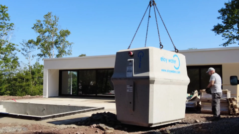 Installation d’une microstation oxyfix® d’eloy en cours de manutention sur le chantier d’une maison individuelle. La cuve est suspendue à un camion-grue, avec un opérateur au levage.