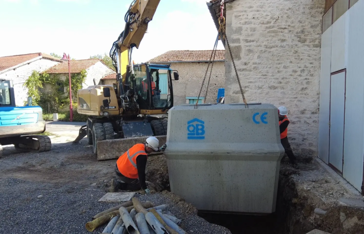 Pose d’une microstation oxyfix® d’eloy dans la fouille d’une allée de garage. La cuve descend à l’aide d’une grue, guidée par deux ouvriers sur le chantier d’une maison individuelle.